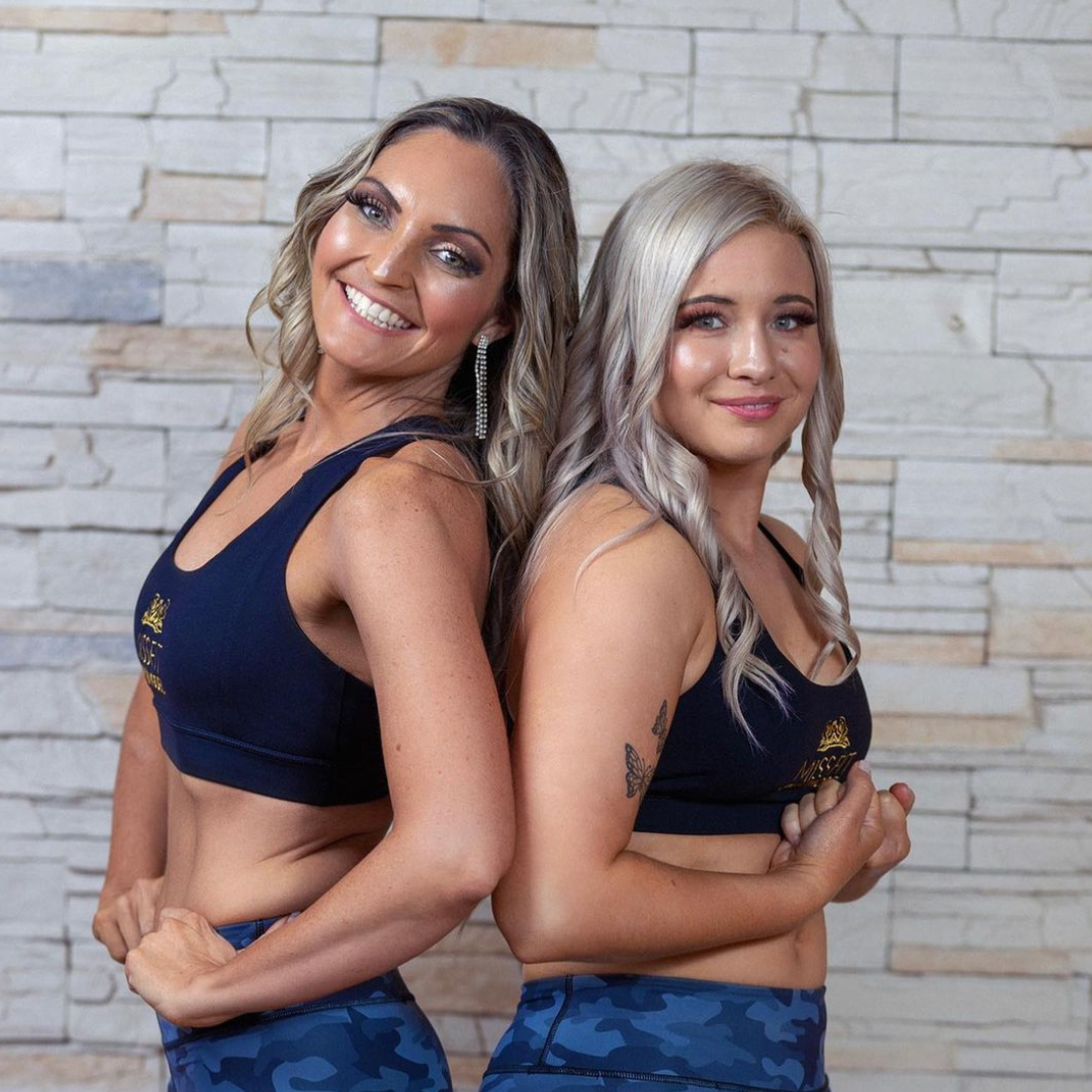 Two women standing back-to-back in navy activewear, showing off their Vibe Classic Brown spray tans.