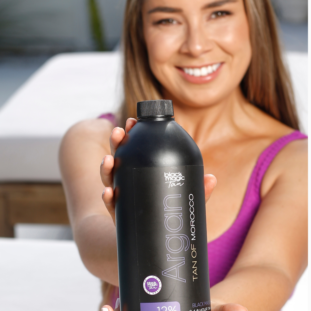 Person holding a bottle of Argan Tan Violet 12% spray tan solution
