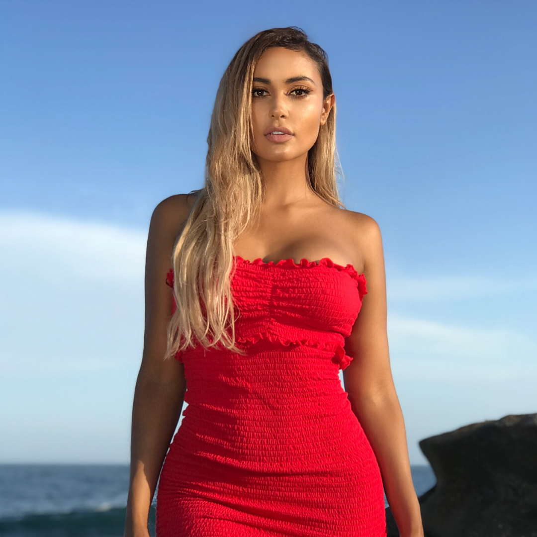 Woman wearing a red dress with a Vibe Rapid Green spray tan standing outdoors by the ocean