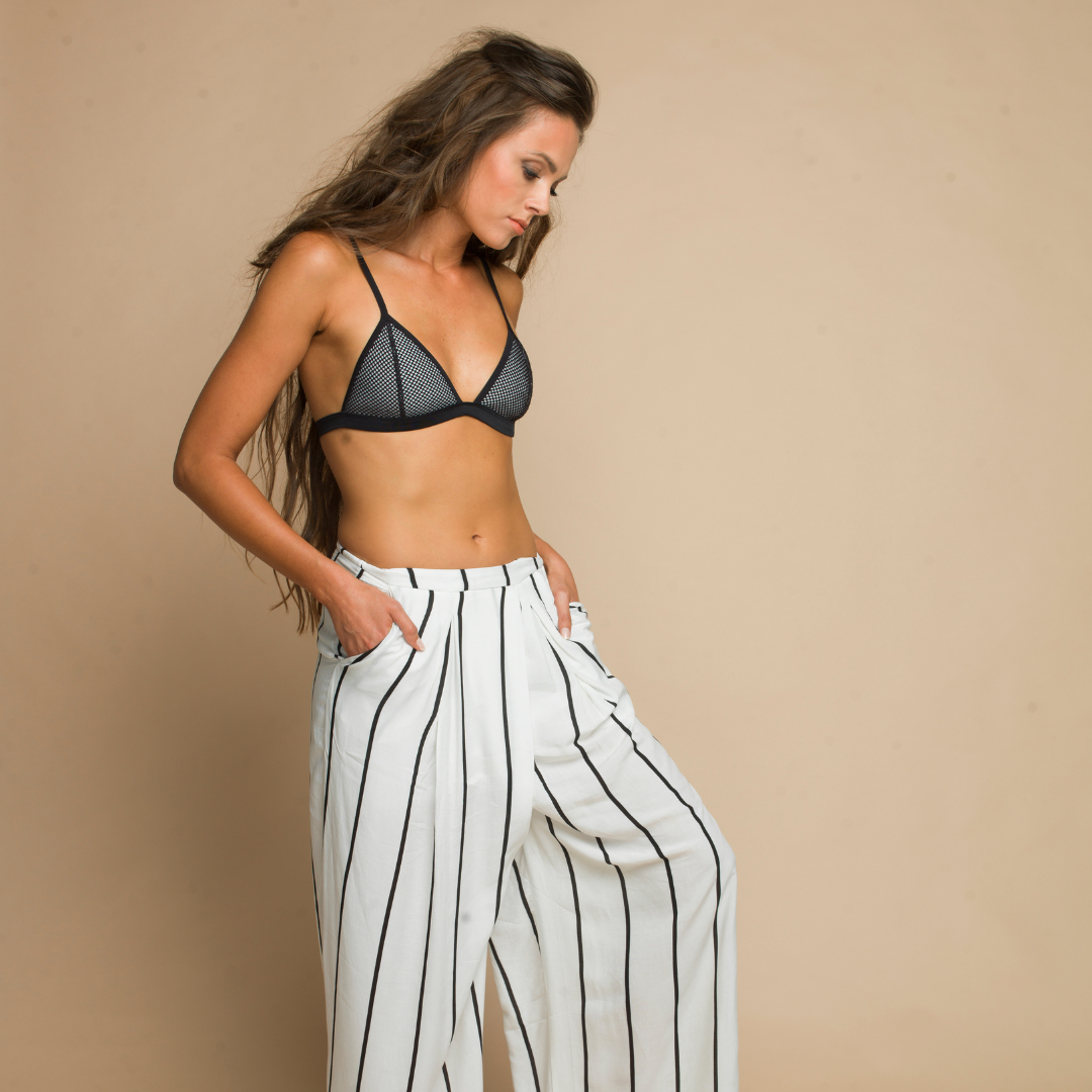 Woman wearing a black bralette and white striped pants looking down, showcasing a Vibe Rapid Violet spray tan with a cool, deep bronze finish.